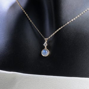 May include: A gold chain necklace with a round blue gemstone pendant. The pendant is set in a gold bezel and has a small diamond accent.