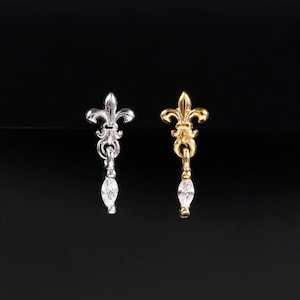 May include: Two stud earrings featuring a fleur-de-lis design. One earring is silver-toned with a clear marquise-cut stone dangling from the base, and the other is gold-toned with an identical clear marquise-cut stone hanging from the bottom.