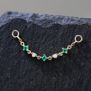 Puede incluir: Una delicada cadena de oro con piedras preciosas verdes esmeralda y blancas. La cadena presenta piedras verdes de talla cuadrada y pequeñas piedras blancas, conectadas por una fina cadena de oro. Tiene un lazo en cada extremo.