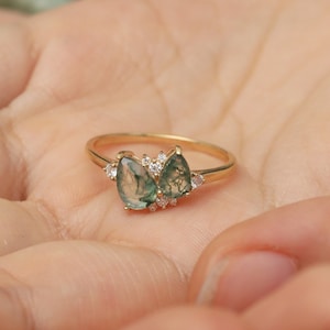 May include: A gold ring with two pear-shaped green gemstones and smaller clear gemstones set in a delicate band.