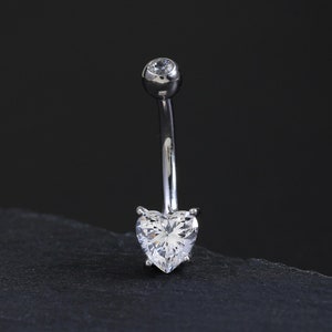 May include: A silver belly button ring with a clear heart-shaped gem.