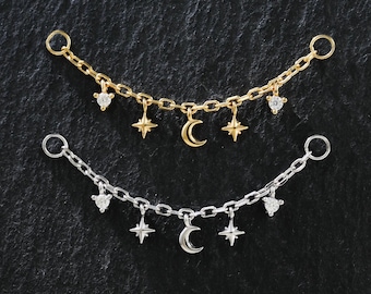 May include: Two celestial-themed jewelry pieces. One is gold-toned, the other silver-toned. Each features a delicate chain with dangling charms, including stars, crescent moons, and heart-shaped accents. The jewelry is displayed against a dark background.