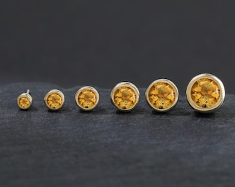 Könnte beinhalten: Eine Reihe von sechs runden Ohrsteckern mit facettierten gelben Citrin-Edelsteinen in glatten Metallfassungen. Die Ohrringe sind in einer Linie von klein nach groß angeordnet und zeigen einen Größenverlauf mit warmen, goldgelben Farbtönen.