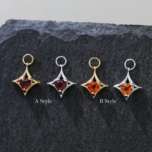 May include: Four gemstone pendants in gold and silver settings. Each pendant features a heart-shaped gemstone within a starburst design. The gemstones are red and orange. The pendants are labelled "A Style" and "B Style".