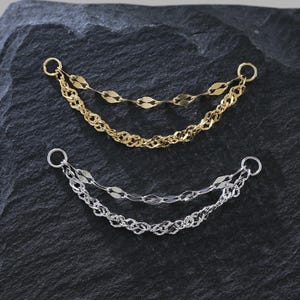 May include: Two layered chain earrings. One pair is gold-toned, featuring a delicate chain and a chain of flat, oval links. The other pair is silver-toned, with a similar design. Both have small hoops at the top for attachment.