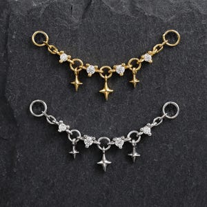 Peut inclure: Deux connecteurs de chaîne de bijoux, un doré et un argenté, chacun présentant un design de chaîne incurvée avec de petites pierres claires et trois breloques en forme d'étoile à quatre branches suspendues aux maillons centraux.