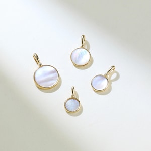 May include: Four gold pendants with white mother-of-pearl round inserts. The pendants are of different sizes.