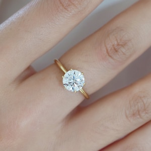 May include: A gold band engagement ring with a large, round, clear diamond.