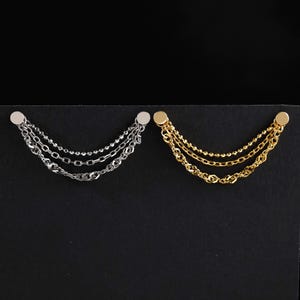 May include: Two multi-strand chain pins, one in silver-tone and one in gold-tone metal. Each pin features two circular studs connected by three distinct draped chain styles, including a beaded chain, a flat link chain, and a twisted chain.