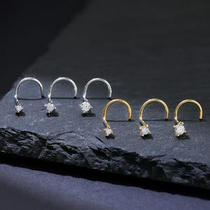 May include: Three pairs of nose rings with small clear gemstones. The rings are made of silver and gold.
