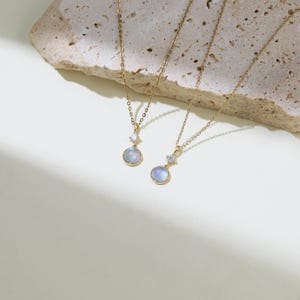 May include: Two gold necklaces with moonstone pendants. Each pendant features a round, iridescent moonstone with a small, clear crystal accent.