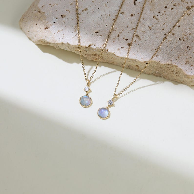 May include: Two gold necklaces with moonstone pendants. Each pendant features a round, iridescent moonstone with a small, clear crystal accent.
