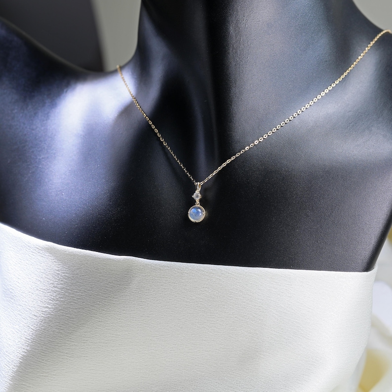 May include: A gold chain necklace with a round blue gemstone pendant. The pendant is set in a gold bezel and has a small diamond accent.