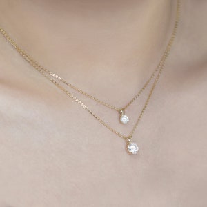 Pu&ograve; includere: Due delicate collane d'oro, ciascuna con un singolo pendente rotondo di diamanti. Le collane sono a strati, con un pendente leggermente pi&ugrave; grande dell'altro. Le catene sono sottili e i diamanti brillano.