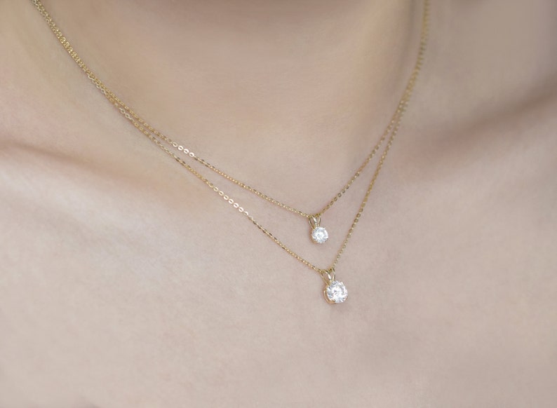 Pu&ograve; includere: Due delicate collane d'oro, ciascuna con un singolo pendente rotondo di diamanti. Le collane sono a strati, con un pendente leggermente pi&ugrave; grande dell'altro. Le catene sono sottili e i diamanti brillano.