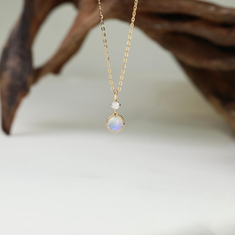May include: A gold chain necklace with a round iridescent moonstone pendant and a smaller clear gemstone above it.