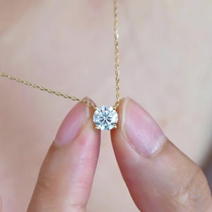 Può includere: Una delicata collana con catenina dorata caratterizzata da una singola pietra preziosa trasparente a taglio brillante rotondo, montata su una base in oro a quattro punte. Il pendente è sospeso a una sottile catena a maglie dorate lucide.