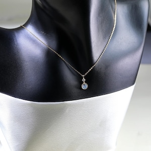 May include: A delicate gold chain necklace with a small round blue gemstone pendant and a smaller clear gemstone above it.