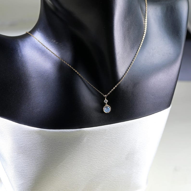 May include: A delicate gold chain necklace with a small round blue gemstone pendant and a smaller clear gemstone above it.
