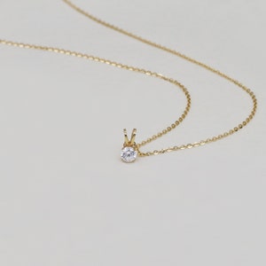 Pu&ograve; includere: Una delicata collana d'oro con un piccolo pendente rotondo di pietra preziosa trasparente. Il pendente &egrave; tenuto da un'incastonatura d'oro e pende da una sottile catena d'oro. La collana &egrave; esposta su uno sfondo morbido e neutro.