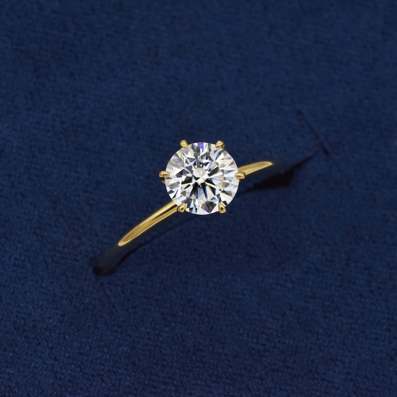 May include: A gold engagement ring with a round, clear diamond.