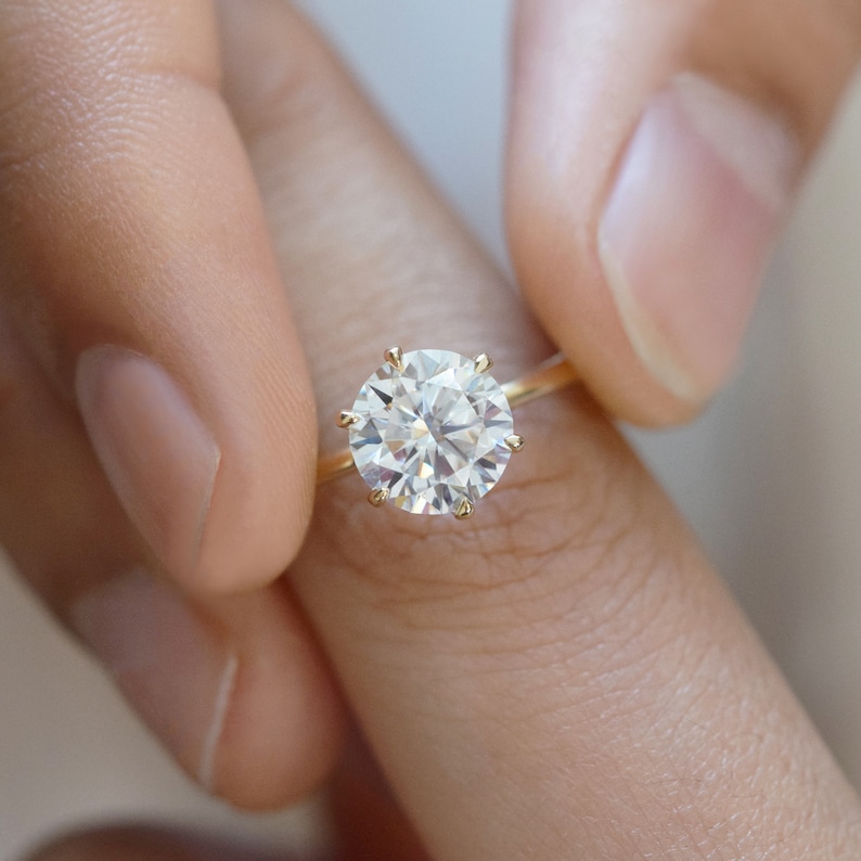 May include: A gold engagement ring with a large, round, clear diamond.