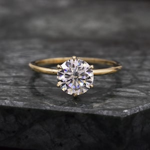 May include: A gold engagement ring with a large, round, clear diamond.