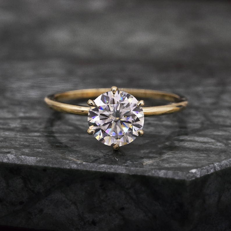 May include: A gold engagement ring with a large, round, clear diamond.