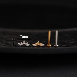 May include: A collection of small, decorative ear studs. Two studs feature a lotus flower design with clear gemstones, measuring 7mm wide and 3mm high. Two additional studs are gold and silver colored, with a flat top.