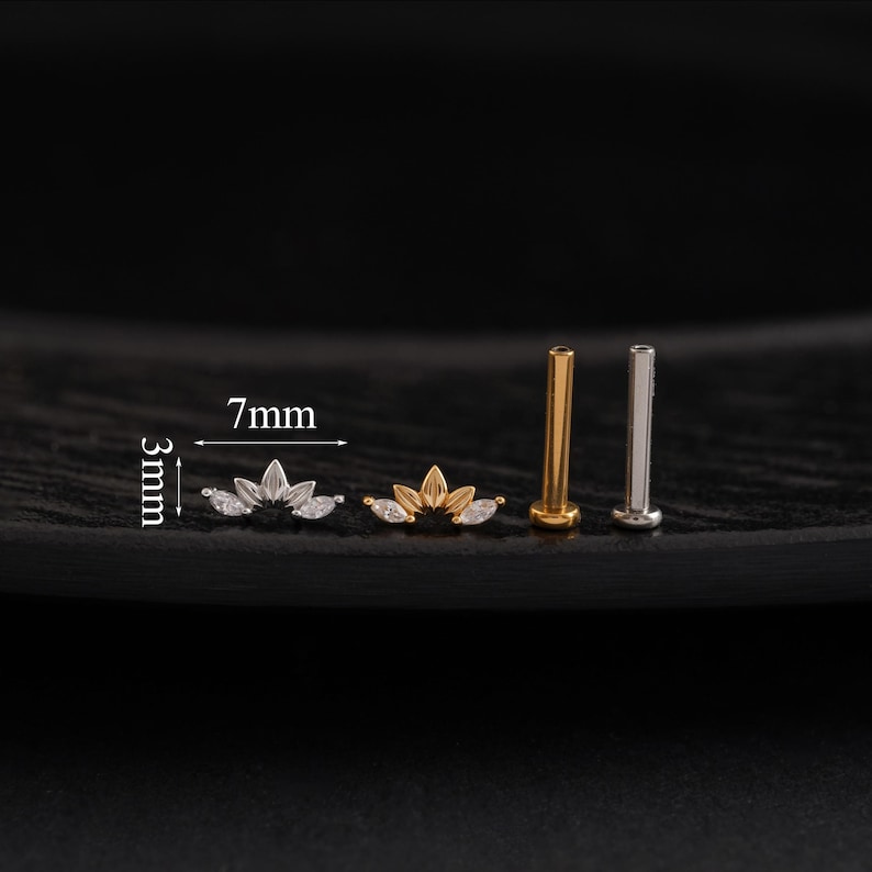 May include: A collection of small, decorative ear studs. Two studs feature a lotus flower design with clear gemstones, measuring 7mm wide and 3mm high. Two additional studs are gold and silver colored, with a flat top.