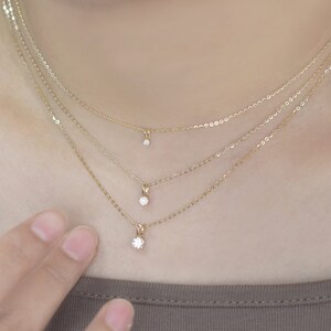 Pu&ograve; includere: Tre delicate collane d'oro, ciascuna con un piccolo e scintillante pendente di diamante. Le collane sono a strati, creando un effetto a pi&ugrave; livelli. Le catene sono sottili e i diamanti sono incastonati in montature semplici ed eleganti. L'estetica generale &egrave; minimalista e raffinata.