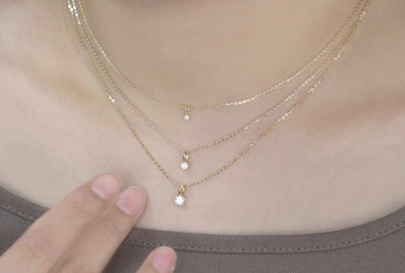 Pu&ograve; includere: Tre delicate collane d'oro, ciascuna con un piccolo e scintillante pendente di diamante. Le collane sono a strati, creando un effetto a pi&ugrave; livelli. Le catene sono sottili e i diamanti sono incastonati in montature semplici ed eleganti. L'estetica generale &egrave; minimalista e raffinata.