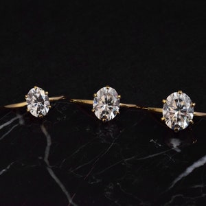 May include: Three gold rings with clear round gemstones on a black marble surface.
