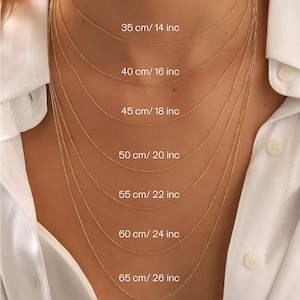 Pu&ograve; includere: Una selezione di delicate collane d'oro di varie lunghezze, presentate su una camicia bianca. Le collane variano da 35 cm a 65 cm, con le corrispondenti misure in pollici. Ogni catena &egrave; finemente realizzata.