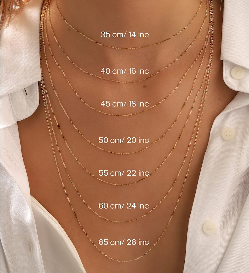 Pu&ograve; includere: Una selezione di delicate collane d'oro di varie lunghezze, presentate su una camicia bianca. Le collane variano da 35 cm a 65 cm, con le corrispondenti misure in pollici. Ogni catena &egrave; finemente realizzata.