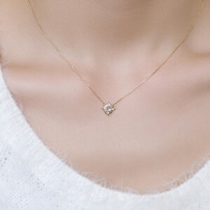 May include: A delicate gold chain necklace featuring a small, starburst-shaped pendant. The center of the pendant contains a single, round, light purple gemstone surrounded by tiny, clear, sparkling stones set in a sunray-inspired metal frame.