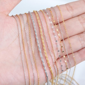 以下が含まれることがあります： さまざまなスタイルと長さの12本の金と銀のチェーンネックレスのコレクション。チェーンは手に表示され、チェーンの端は下に垂れ下がっています。