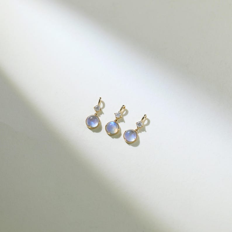 May include: Three gold pendant charms with a round, iridescent blue gemstone and a small, clear crystal accent.