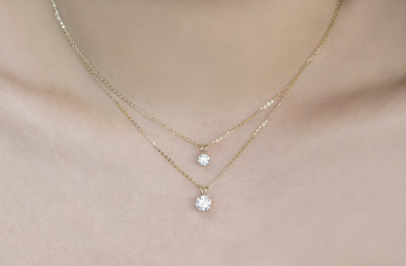 Pu&ograve; includere: Due delicate collane d'oro, ciascuna con un singolo pendente rotondo in pietra preziosa trasparente. Le collane sono a strati, con un pendente leggermente pi&ugrave; piccolo dell'altro. Le catene e i pendenti hanno una finitura lucida e lucidata.