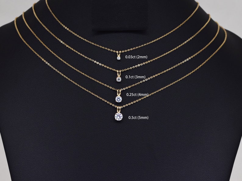 Pu&ograve; includere: Quattro collane d'oro con pendenti di diamanti di varie dimensioni sono esposte su sfondo nero. I pendenti sono etichettati con il loro peso in carati e le dimensioni in mm: 0,03 ct (2 mm), 0,1 ct (3 mm), 0,25 ct (4 mm) e 0,5 ct (5 mm).