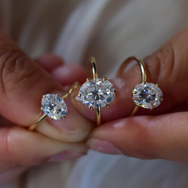 May include: Three gold rings with oval-shaped diamonds. The rings are different sizes, with the largest ring in the center.