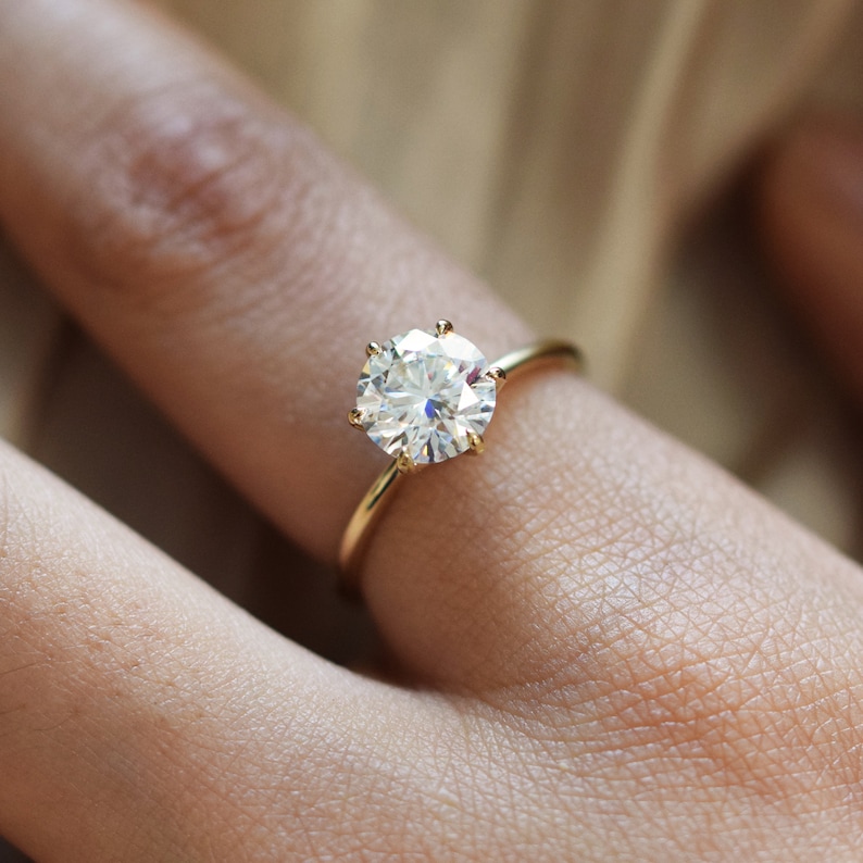 May include: A gold ring with a large, round, clear diamond solitaire.