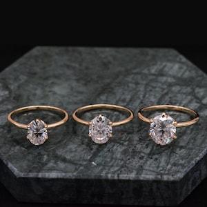 May include: Three gold rings with oval-shaped diamonds set in a prong setting. The rings are arranged in a row from smallest to largest.