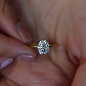 May include: A gold ring with a large, clear oval-shaped diamond.