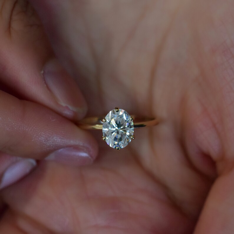 May include: A gold ring with a large, clear oval-shaped diamond.