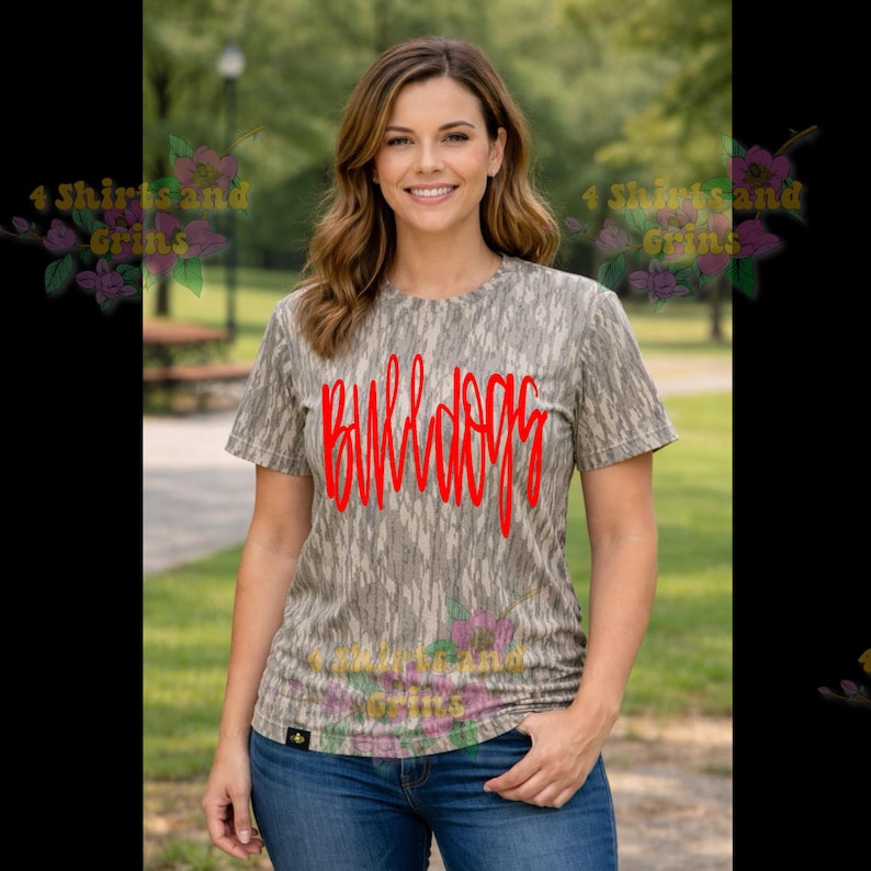 May include: A short-sleeved, crew neck t-shirt with a camouflage pattern in shades of gray and brown. The word "BULLDOGS" is written in red across the front. The person in the image is wearing blue jeans.