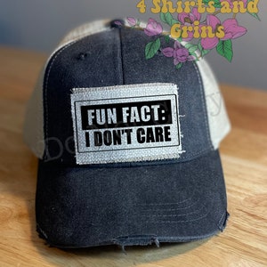 May include: A black and white trucker hat with a distressed look. The hat has a patch sewn on the front that says "Fun Fact: I Don't Care".