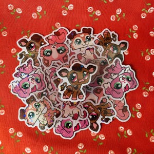 May include: A collection of colorful, glittery animal stickers. The stickers feature various animals, including a cow, a dog, a cat, and a pig. The stickers are all in a cartoon style and have a whimsical feel.