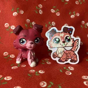 May include: Two pink and white dog figurines. One is a 3D printed figurine and the other is a sticker. Both dogs have sparkly eyes.