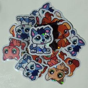May include: A collection of holographic stickers featuring cartoon puppies in various poses. The stickers are on a white background and feature a variety of colors, including blue, red, orange, and brown.